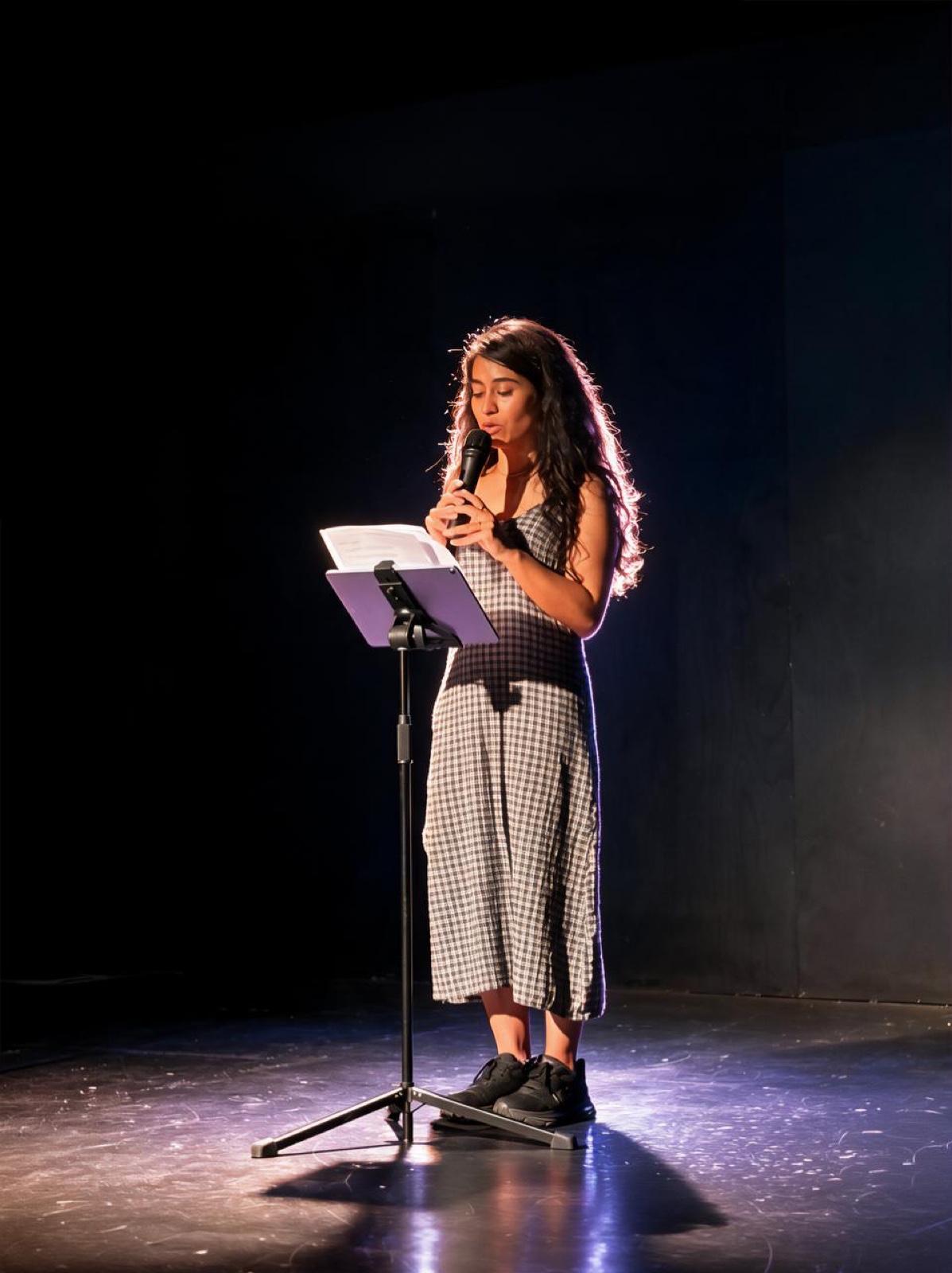 Gurmeet Kaur reading on stage under a spotlight